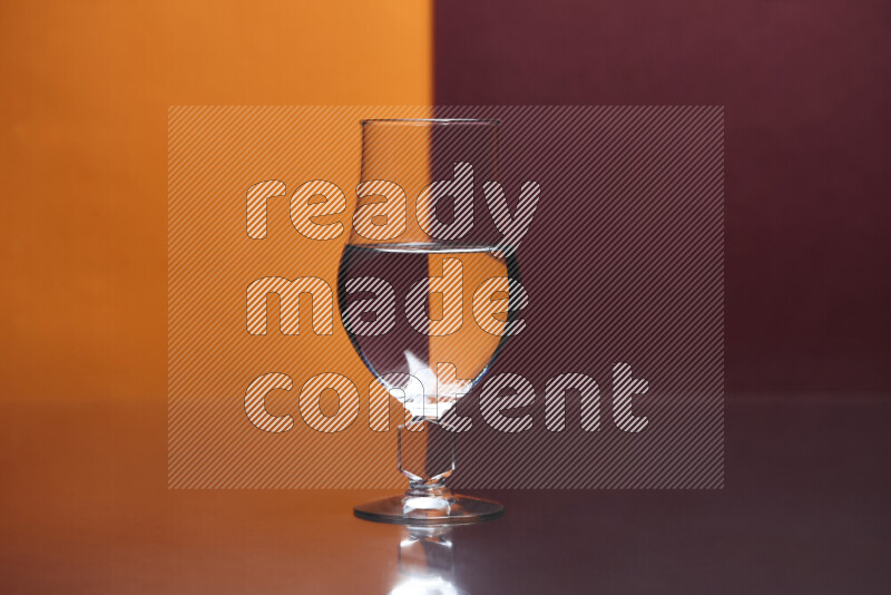 The image features a clear glassware filled with water, set against orange and dark red background