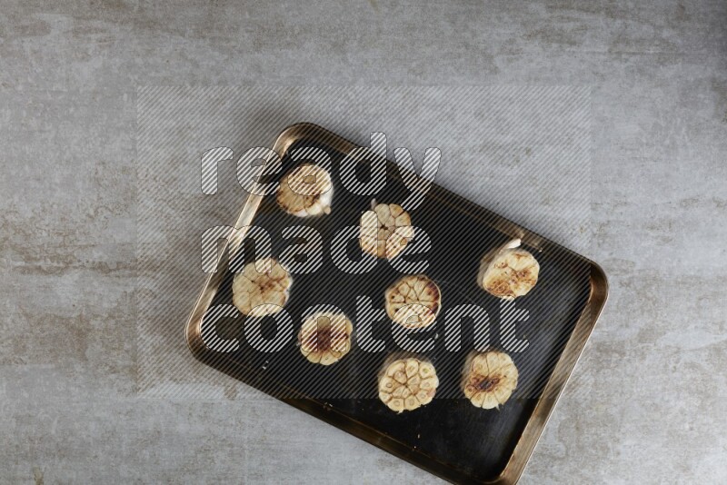 half's roasted garlic in a stainless tray on a grey textured countertop