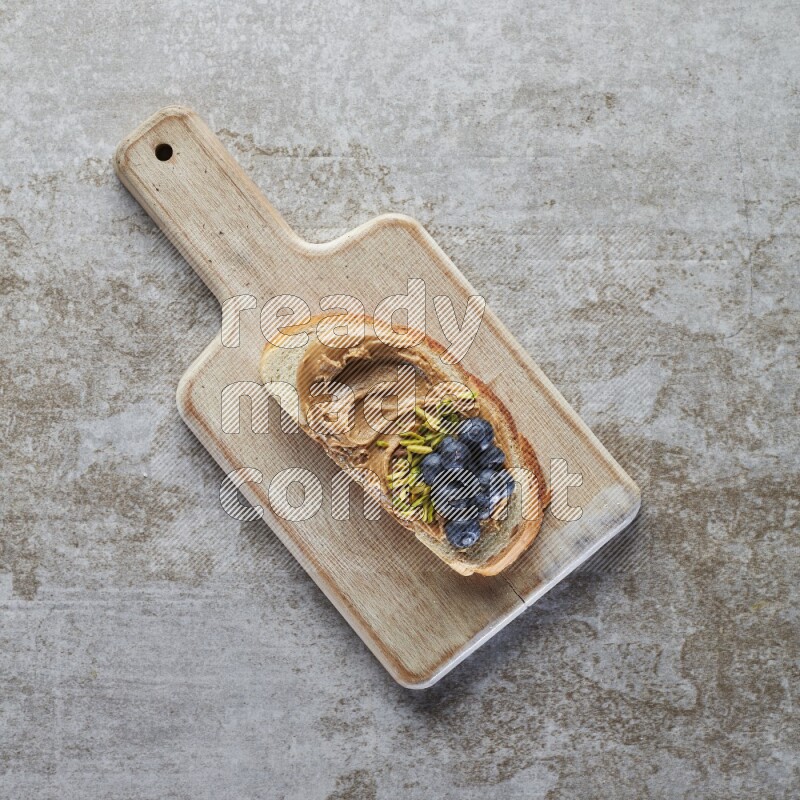open faced peanut butter sandwich with blueberries and pistachio on a grey textured background