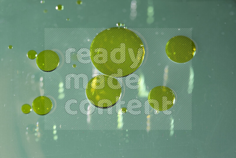 Close-ups of abstract yellow watercolor drops on oil Surface on green background