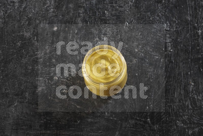 A glass jar full of mustard paste on a textured black flooring