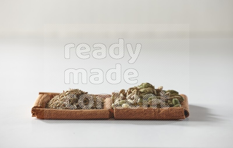 مربعان من أعواد القرفة ممتلئان بحبوب الهيل والكمون علي خلفية بيضاء