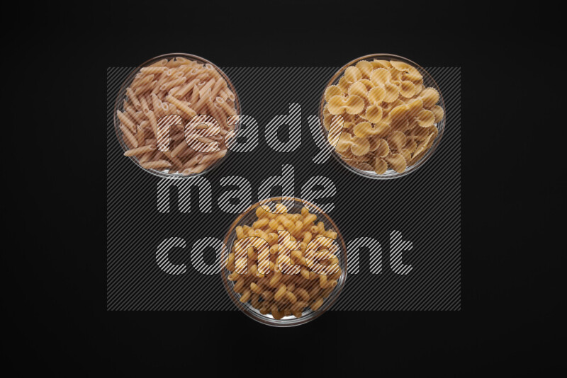 Different pasta types in glass bowls on black background