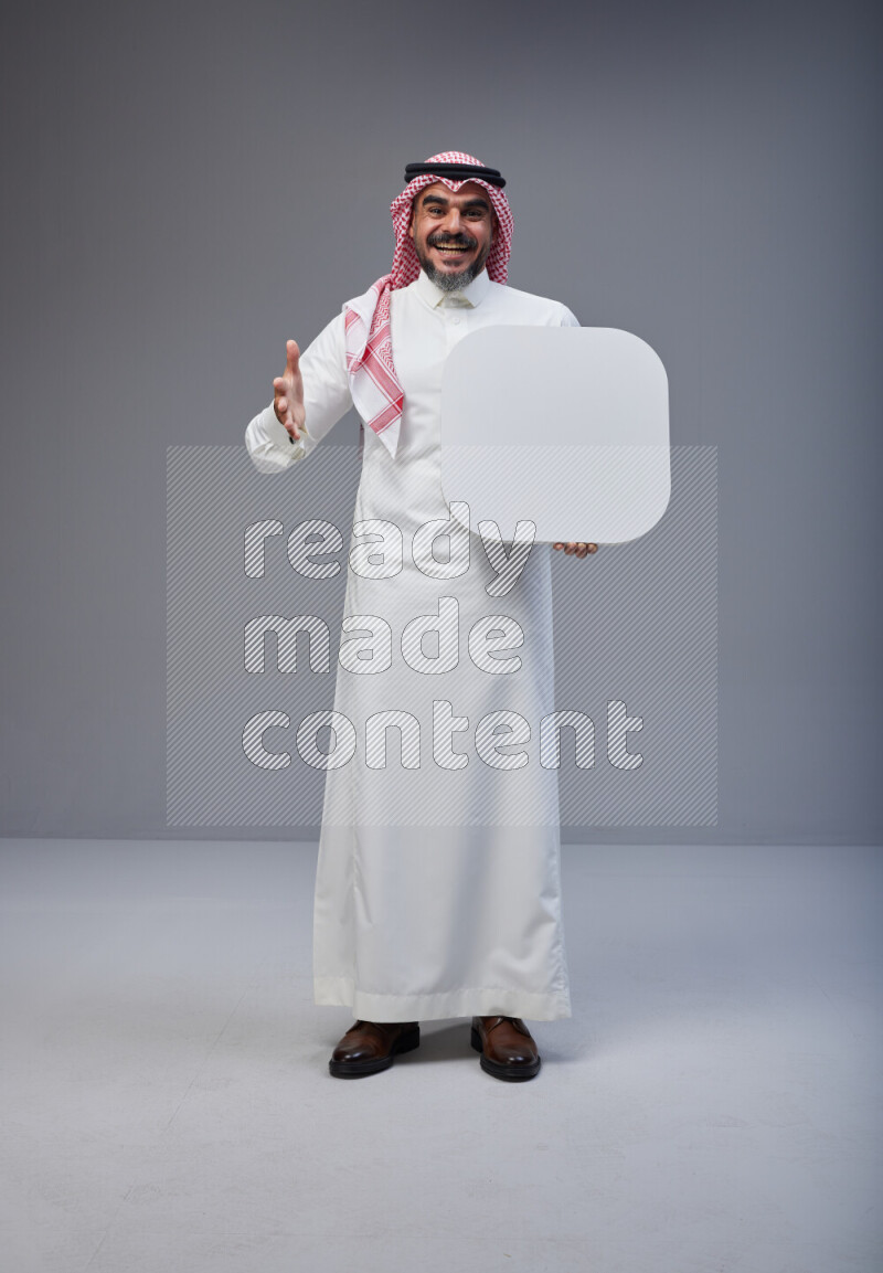 Saudi man Wearing Thob and red Shomag standing holding social media sign on Gray background