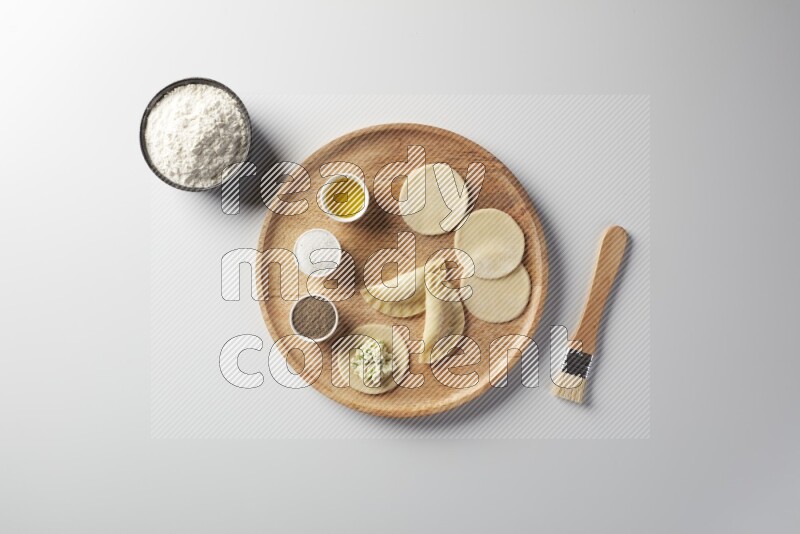 two closed sambosas and one open sambosa filled with cheese while flour, salt, black pepper and oil with oil brush aside in a wooden dish on a white background
