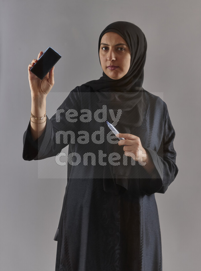 Woman in black abaya and hijab holding a marker pen to write on a transparent board with different reactions and expressions on grey background