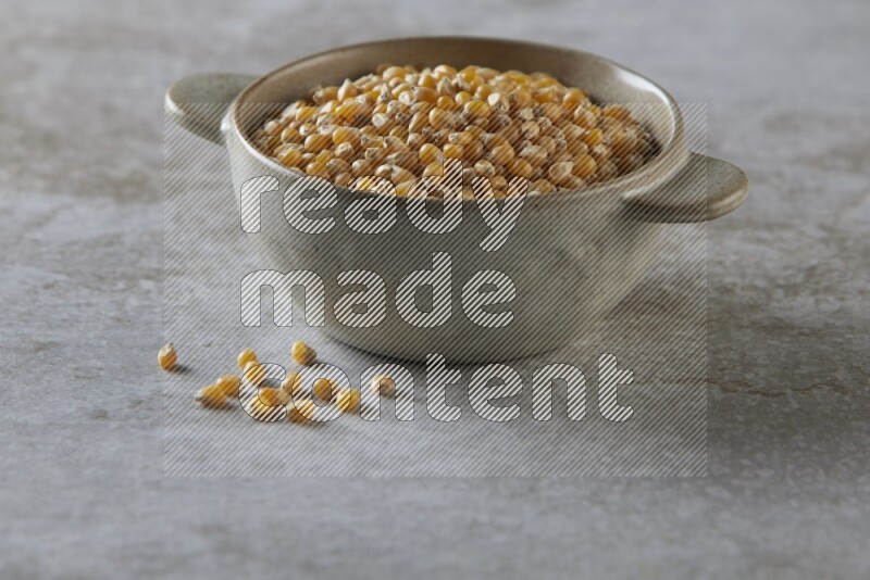 corn kernel in a off-white handheld ceramic bowl on a grey textured countertop
