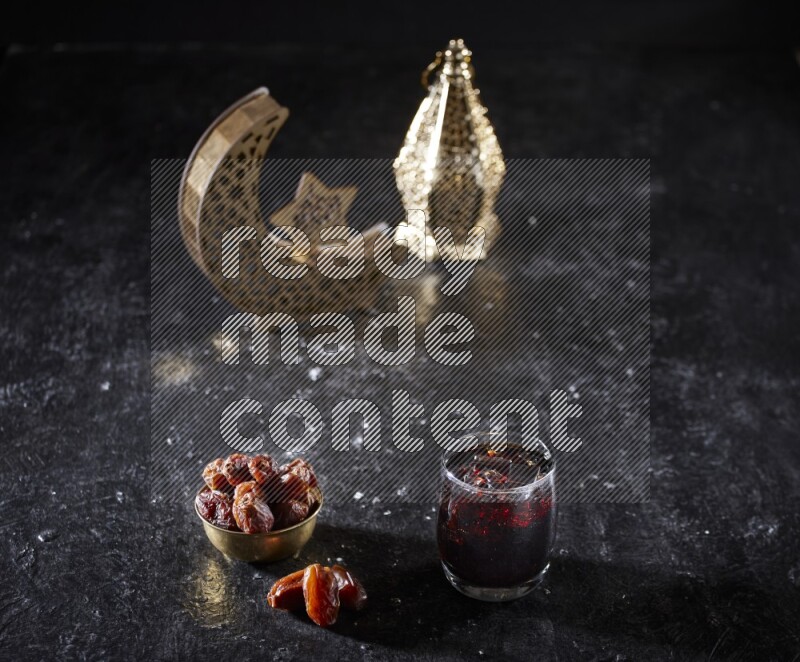 Dates in a metal bowl and tamarand beside a gold crescent and a lantern in a dark setup