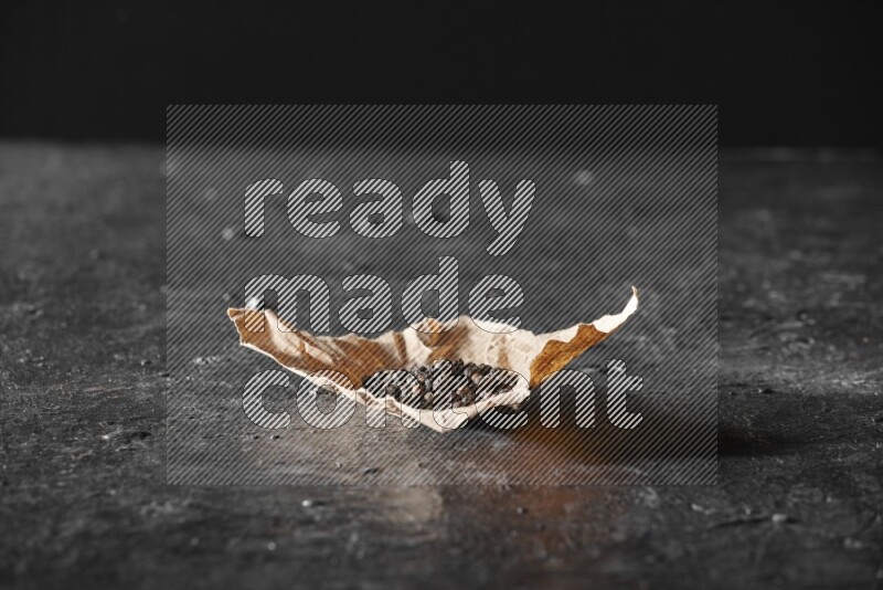 حبوب الفلفل الأسود في قطعة من الورق علي خلفية سوداء