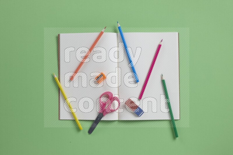 A blank open notebook with different school supplies on green background