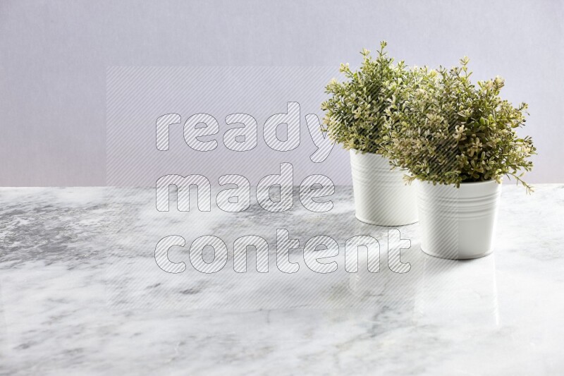 Two green artificial plants in white pot on grey marble background