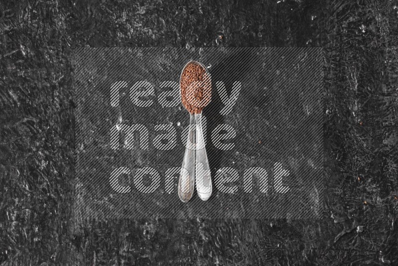 2 metal spoons full of garden cress seeds on a textured black flooring