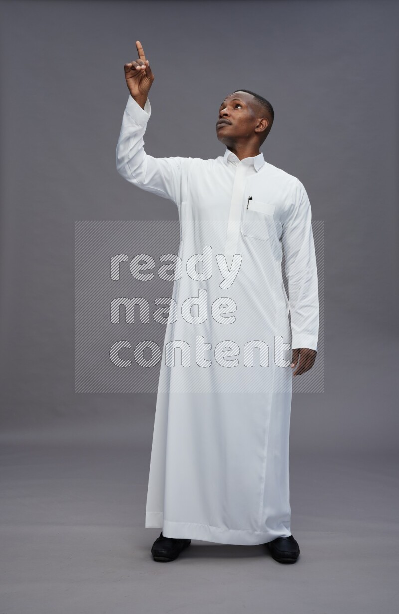 Saudi man wearing thob standing interacting with the camera on gray background