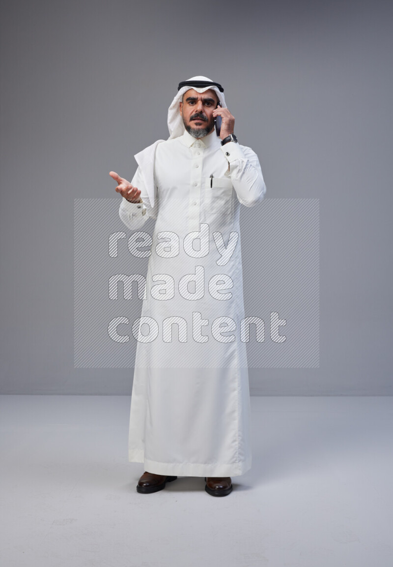 Saudi man Wearing Thob and white Shomag standing talking on phone on Gray background