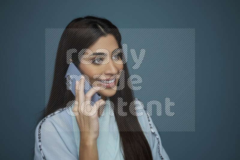 A Saudi woman having a Call in a blue background wearing a blue Abaya with no hijab