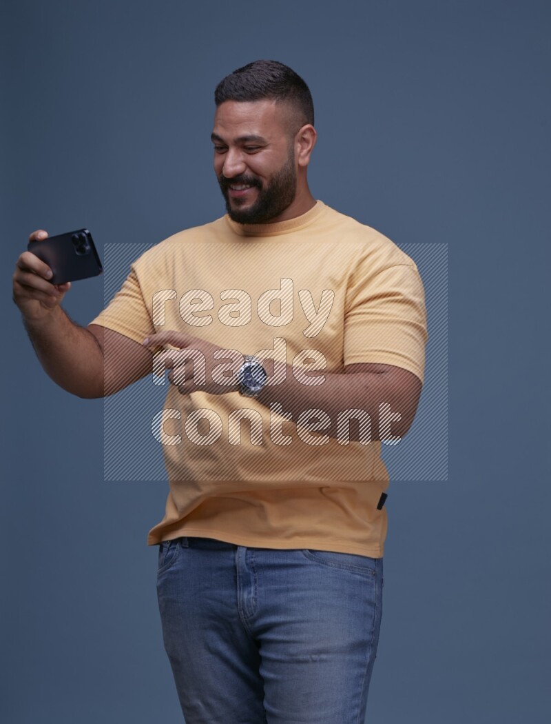 A man Playing Games on Smartphone on Blue Background wearing Orange T-shirt