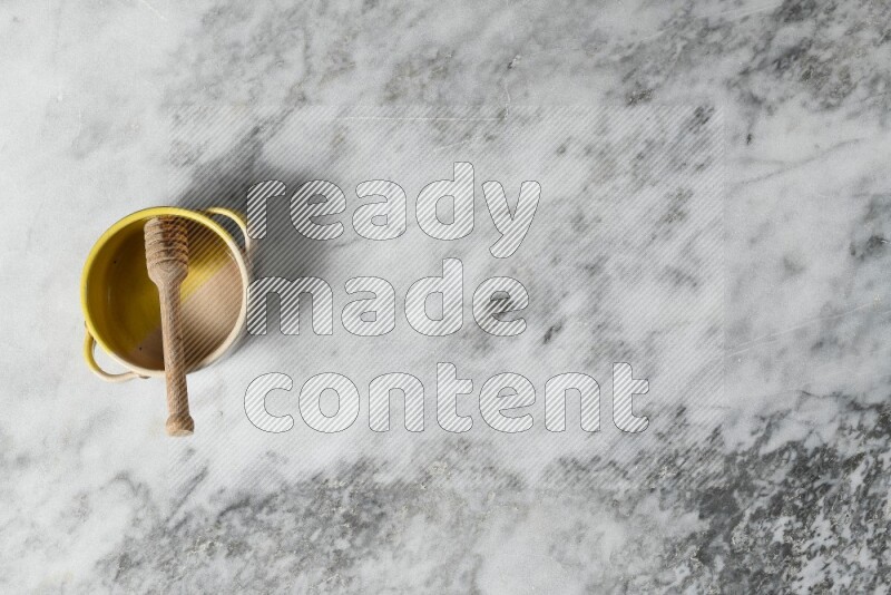 Multicolored pottery bowl with wooden honey dipper in it on grey marble background