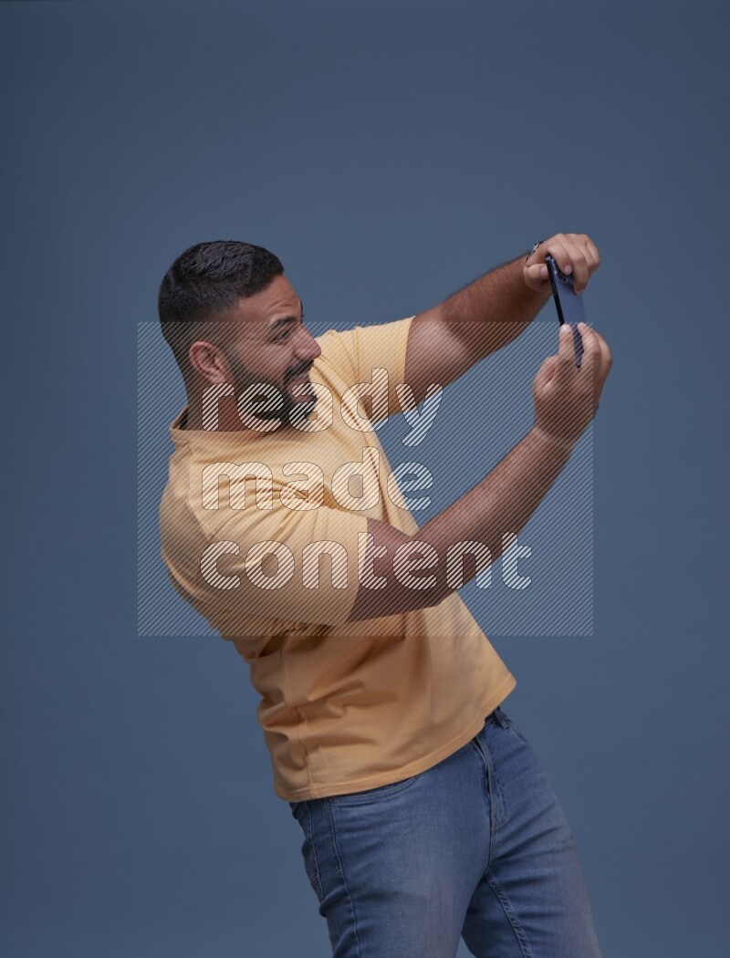 A man Playing Games on Smartphone on Blue Background wearing Orange T-shirt