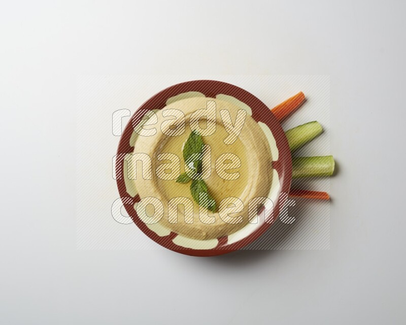 Hummus in a traditional plate garnished with mint on a white background