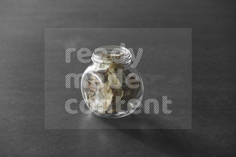 A glass spice jar full of bay laurel leaves on black flooring