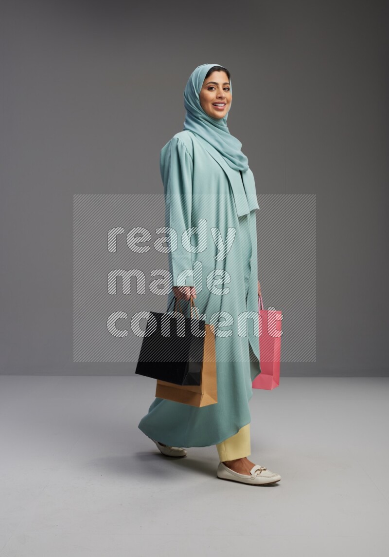 Saudi Woman wearing Abaya standing holding shopping bag on Gray background