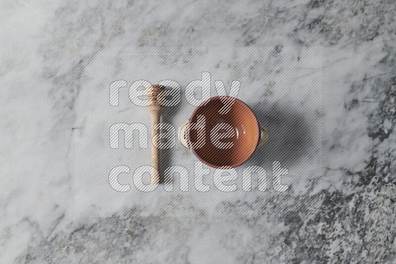 Brown pottery bowl with wooden honey dipper on the side on grey marble background