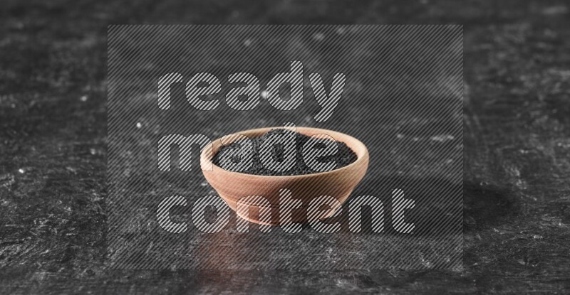 A wooden bowl full of black seeds on a textured black flooring