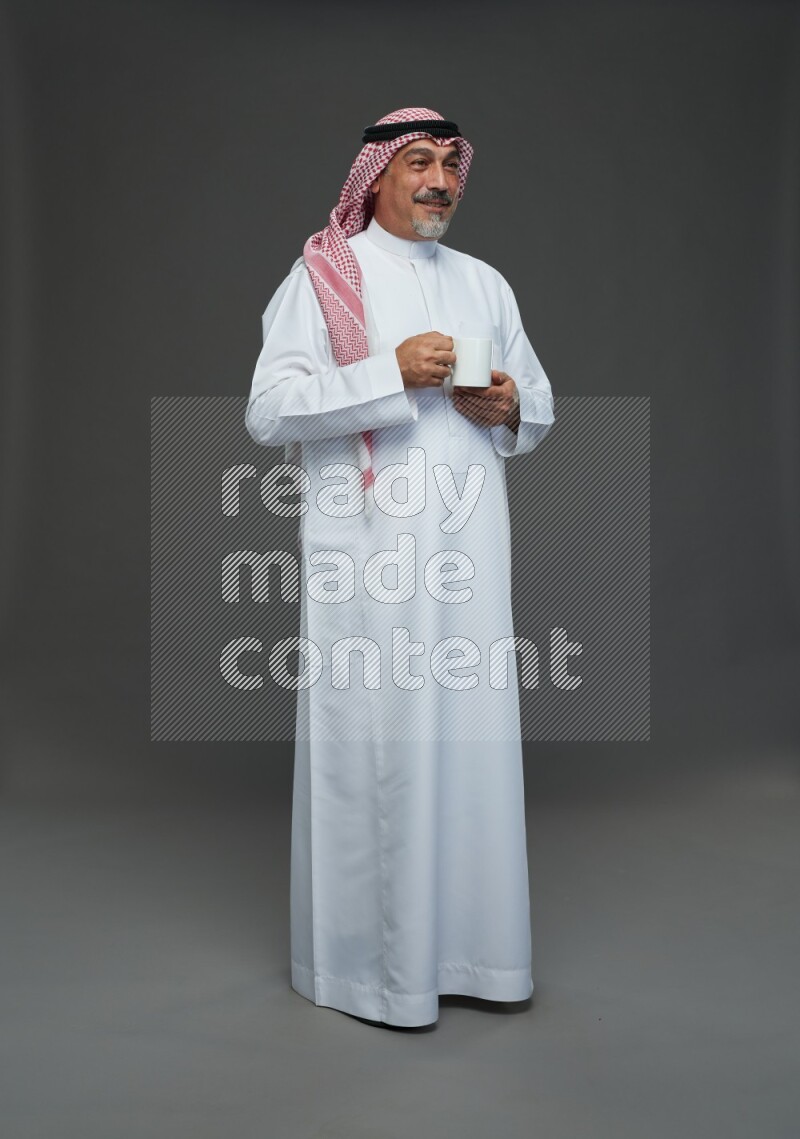 Saudi man with shomag Standing holding mug on gray background