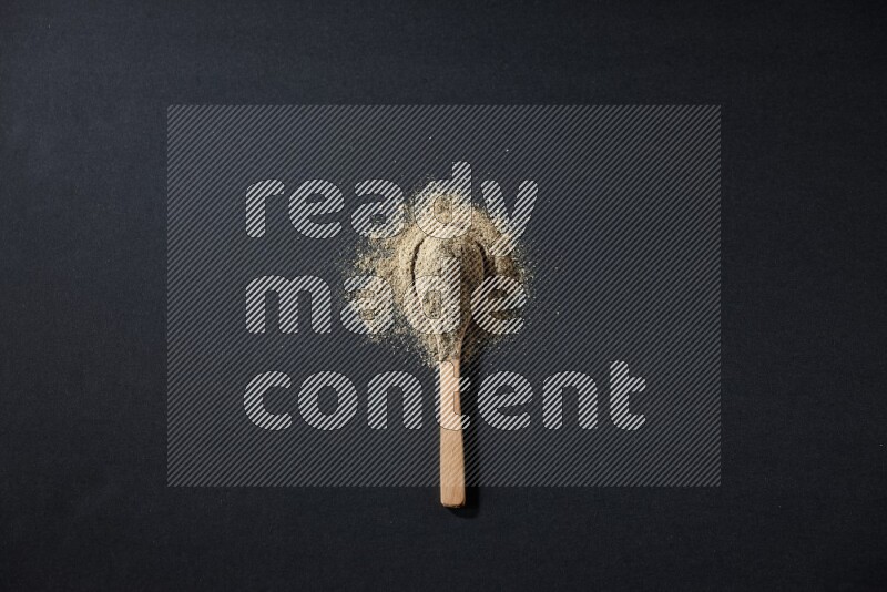 A wooden spoon full of cardamom powder and powder spreaded on black flooring