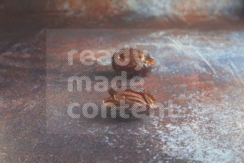 two pecan stuffed madjoul dates on a rustic reddish background