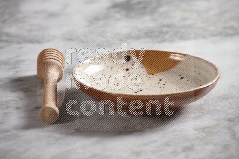 Multicolored pottery plate with wooden honey dipper on the side on grey marble background
