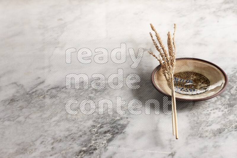 Wheat stalks on decorative pottery plate on grey marble background