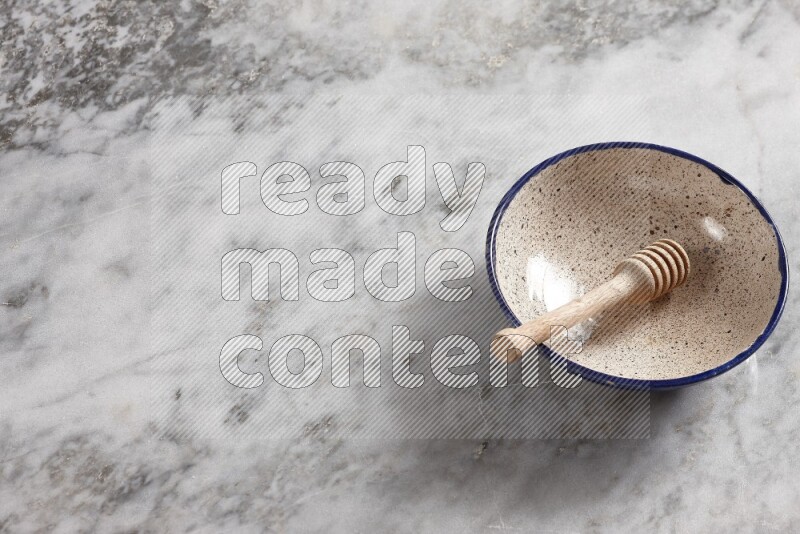 Multicolored pottery bowl with wooden honey dipper in it on grey marble background