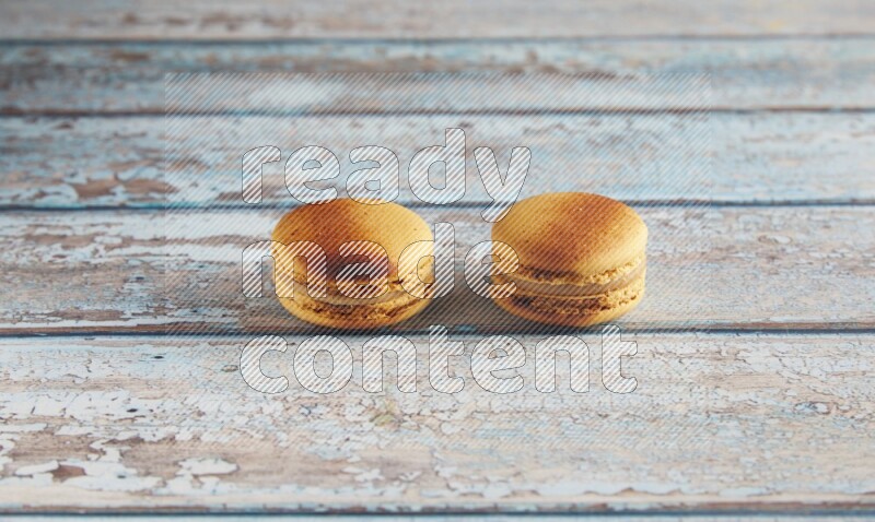45º Shot of two Yellow Crème Brulée macarons on light blue wooden background