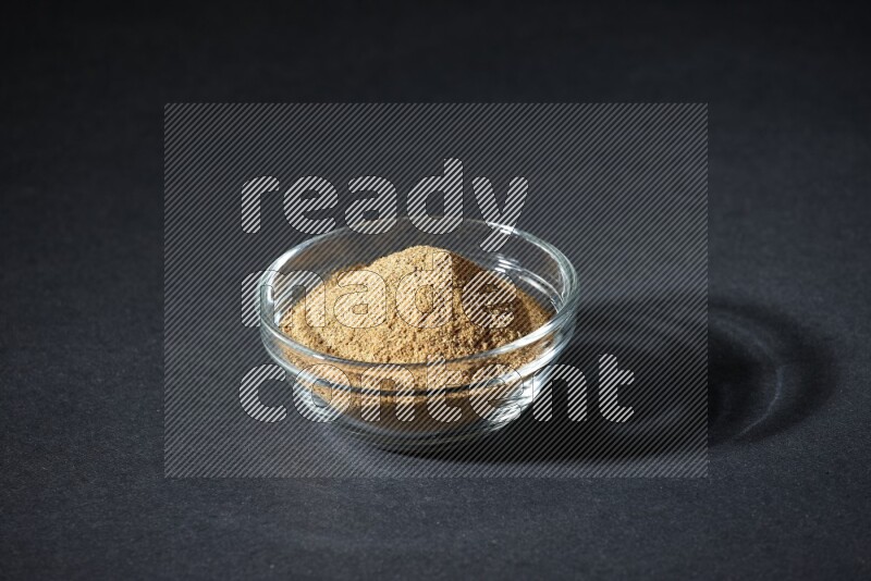 A glass bowl full of cumin powder on black flooring