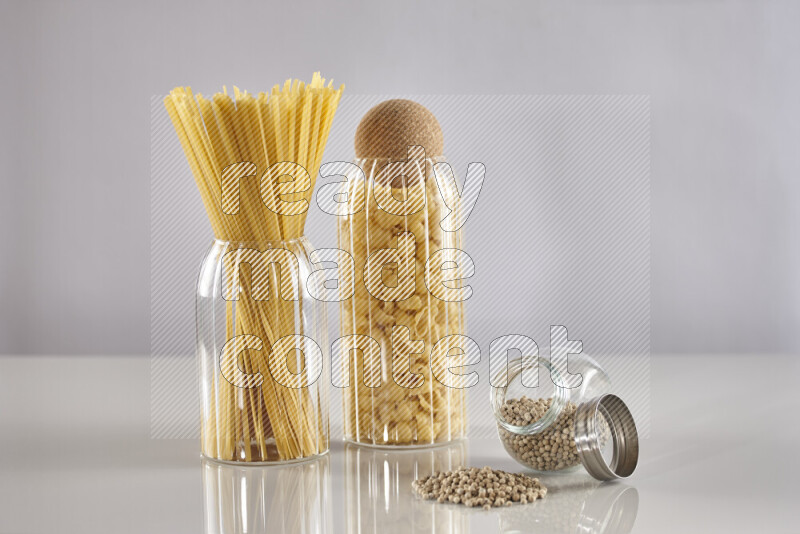 Raw pasta in glass jars with white peppers on light grey background