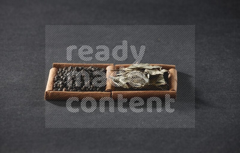 مربعان من أعواد القرفة ممتلئان بحبوب الفلفل الأسود وأوراق الغار علي خلفية سوداء