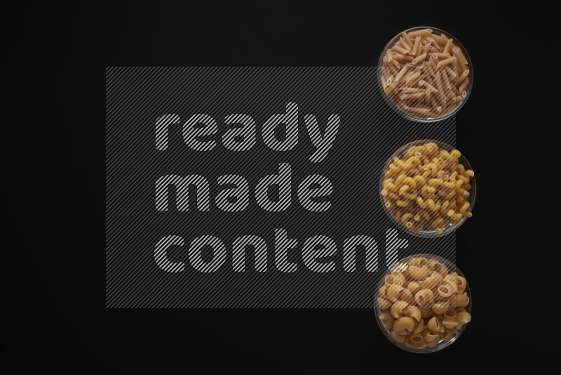 Different pasta types in 3 glass bowls on black background