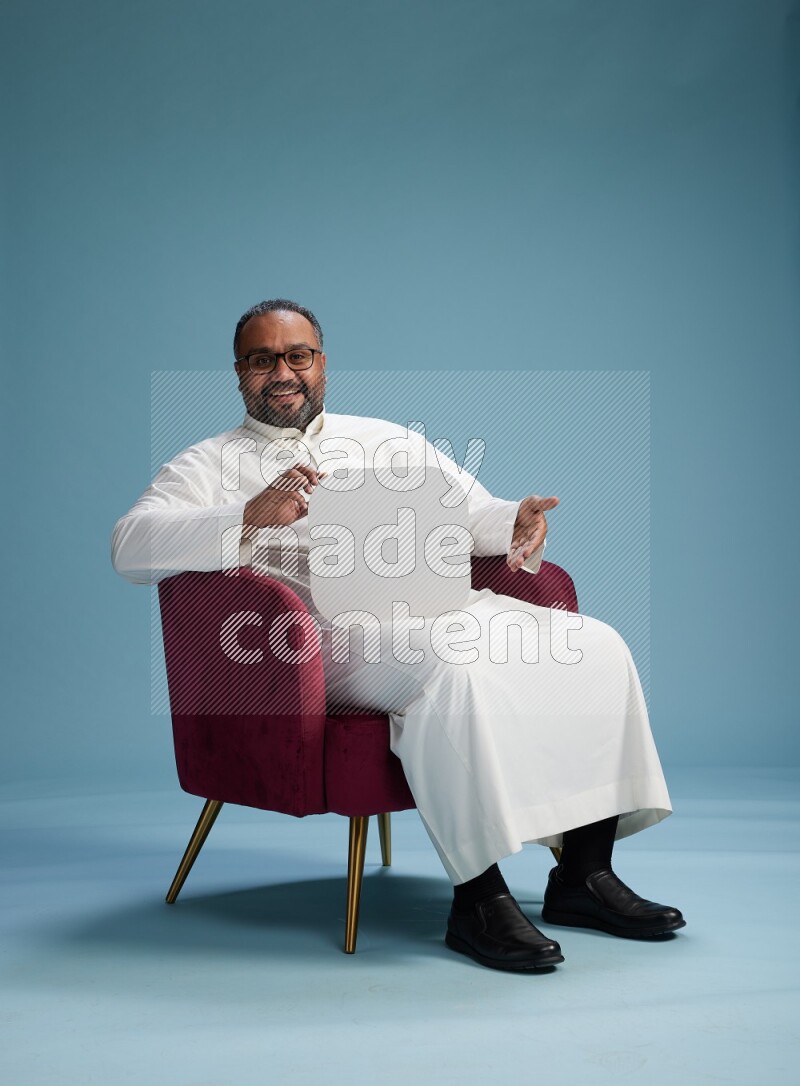 Saudi Man without shimag sitting on chair holding social media sign on blue background
